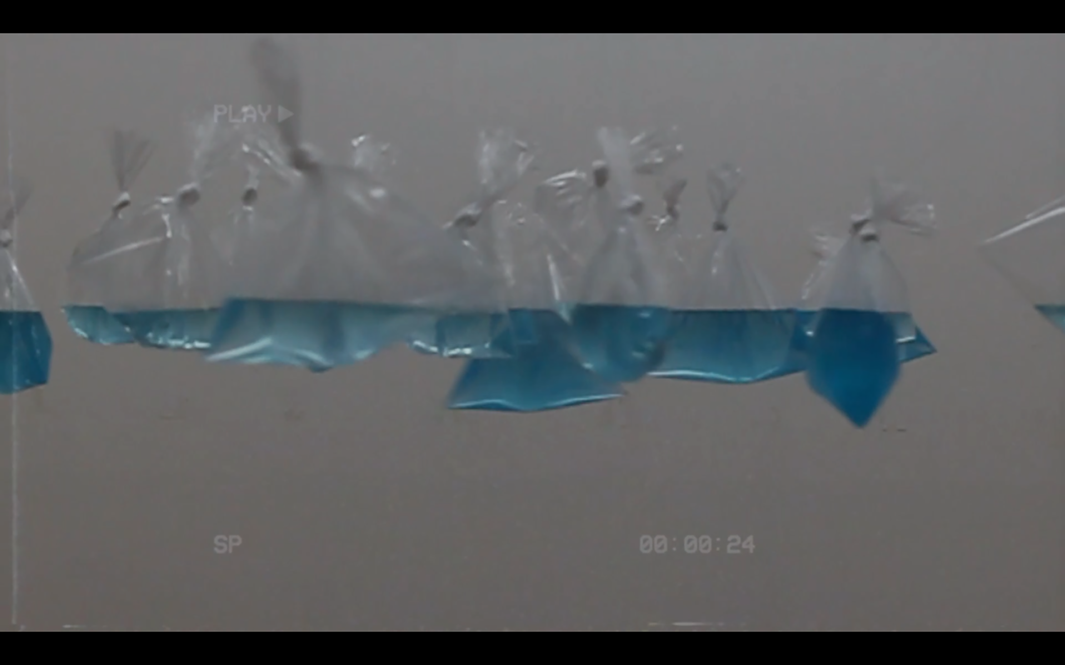 bags of blue water hang in front of a white wall so that they form a horizon line.